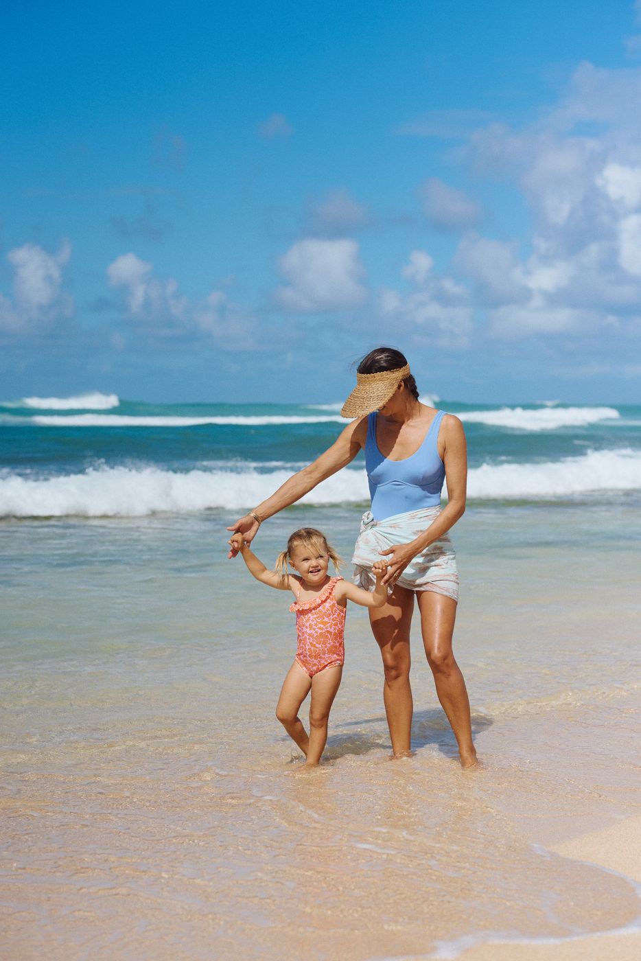 A mother holding her toddler's hands as she plays in the shallows